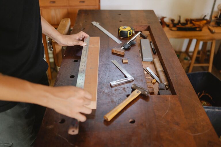 Werkbank mit Zollstock, Holzplatte und einer bemaßten Zeichnung neben einem Laptop