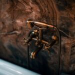 dornbracht - Elegant brass faucet fixture with a luxurious marble wall background.