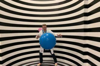 illuseum berlin - A man wearing a lab coat poses with a blue ball in a striped illusion room.